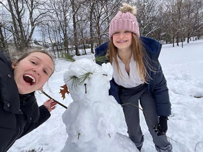 Fachkraft und Gastkind bauen zusammen einen Schneemann