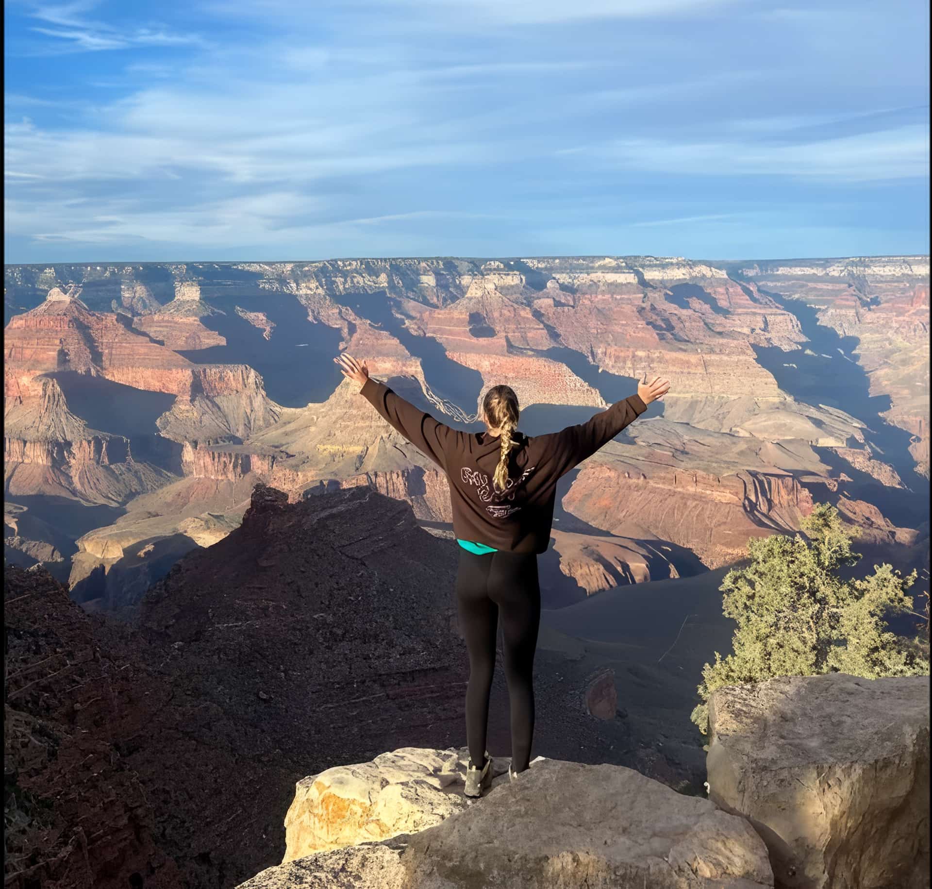 Apex-Social-Teilnehmerin steht mit ausgebreiteten Armen am Rand des Grand Canyon